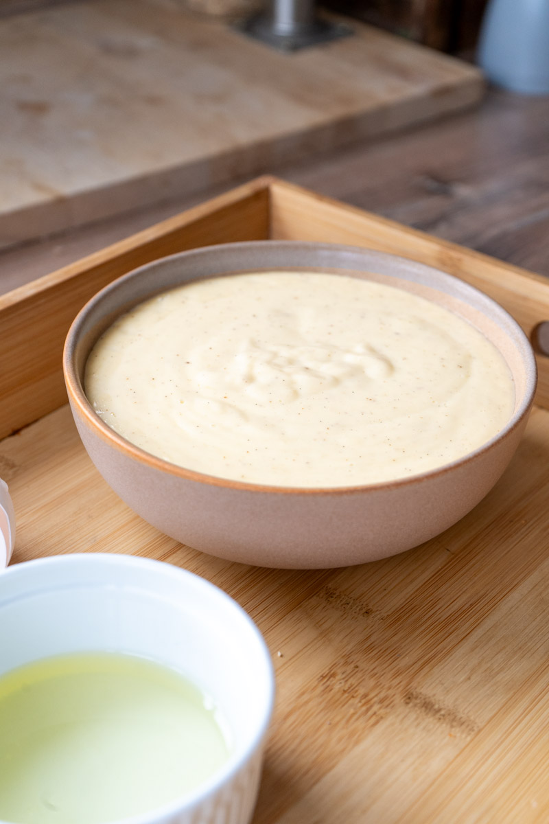 Vanillesauce-2 Schüssel mit Vanillepudding auf einem Holztablett, daneben eine kleinere Schüssel mit einer hellen Flüssigkeit.