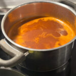 Ein Topf mit rotbrauner Suppe oder Soße auf einem Herd.