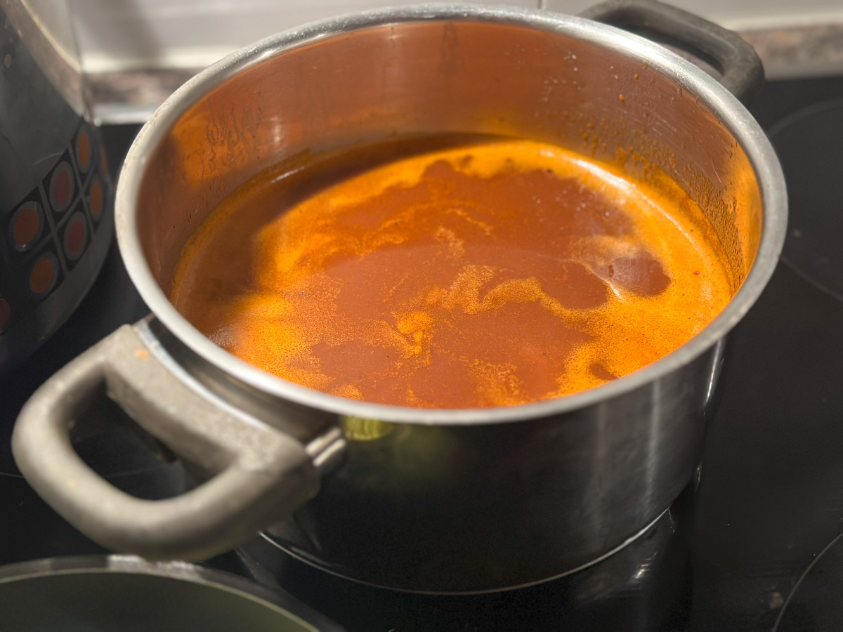 Vegane-Bratensauce-6 Topf mit kochender, roter Suppe auf einem Herd.