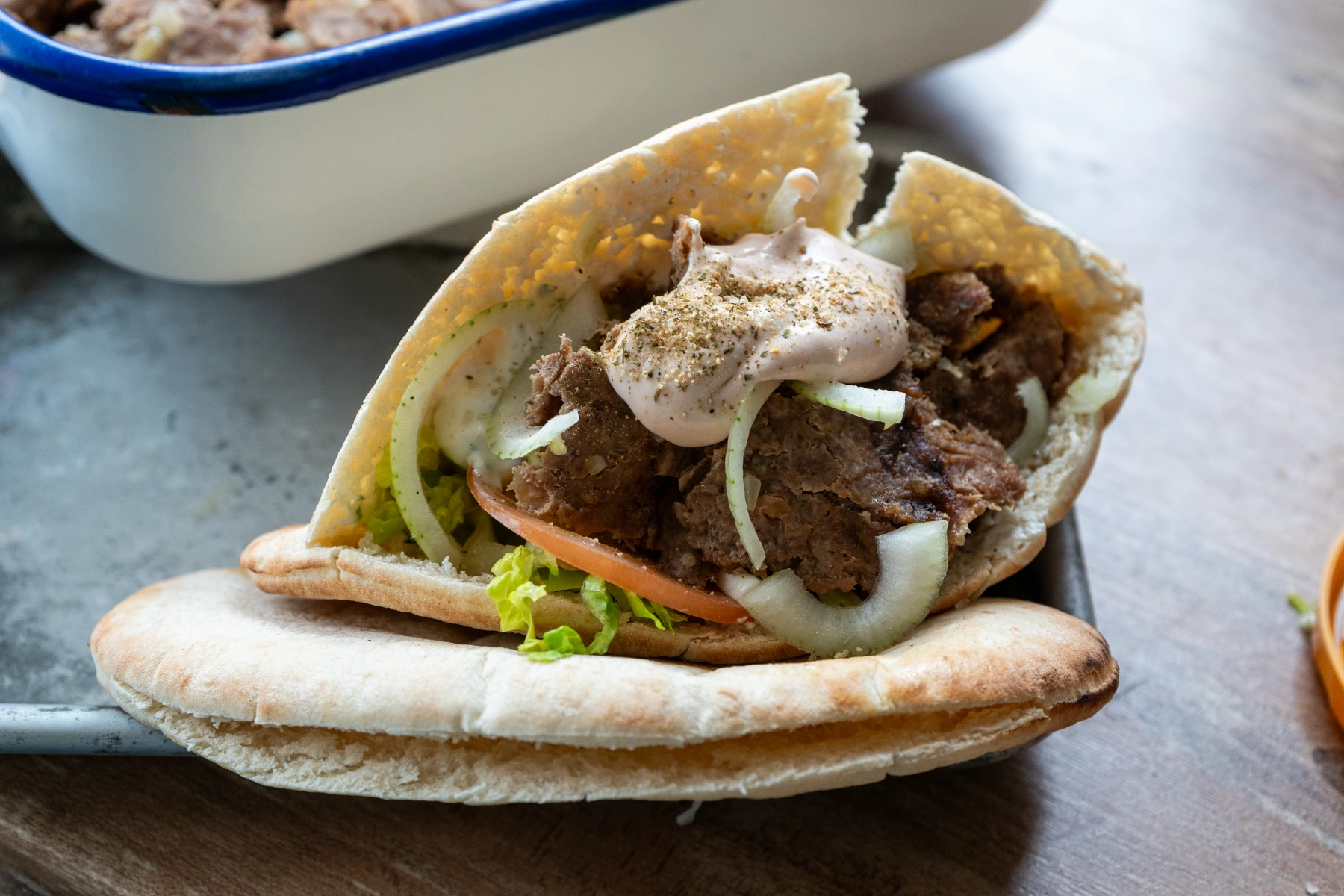 Pita-Tasche mit gegrilltem Fleisch, Zwiebeln, Tomaten, Salat und Sauce gefüllt, auf einem Holzbrett serviert.