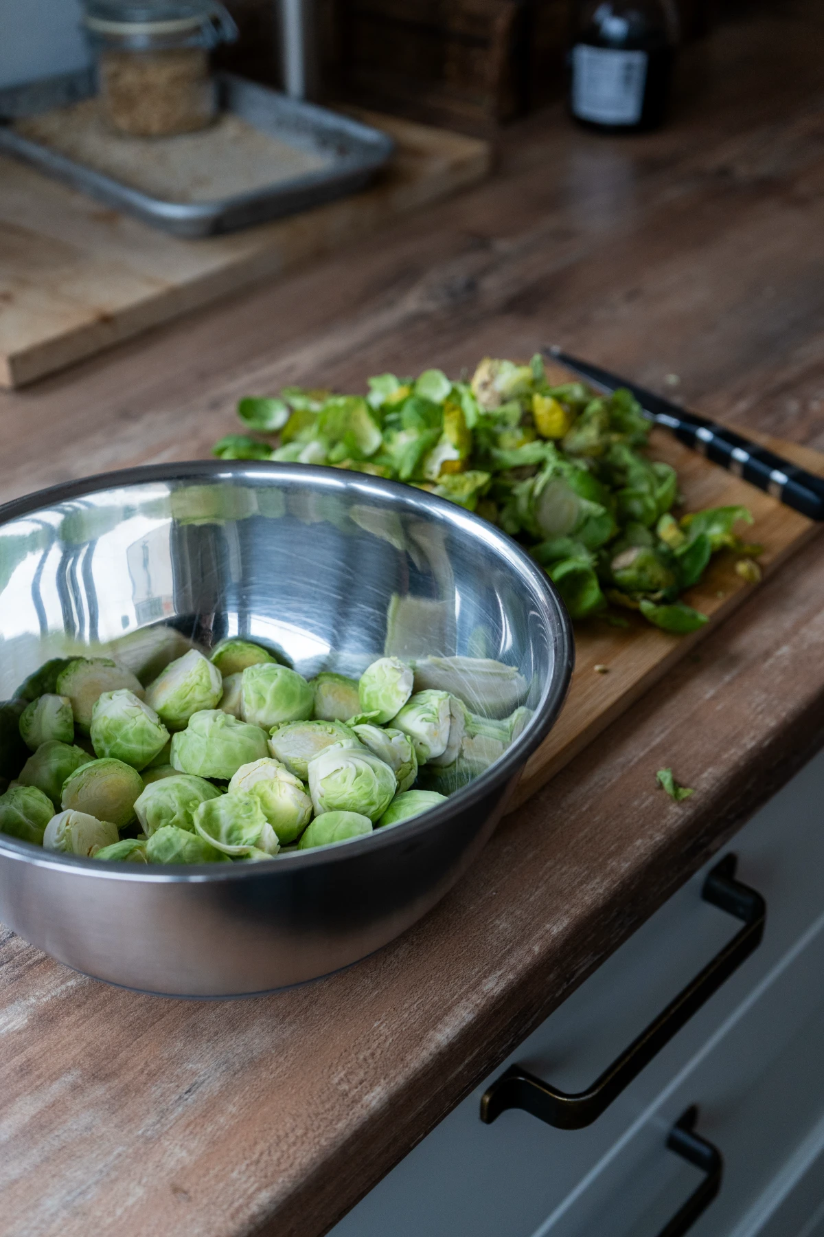 Rosenkohl in einer Metallschüssel auf einem Holztisch, daneben geschnittene Rosenkohlblätter und ein Messer auf einem Schneidebrett.