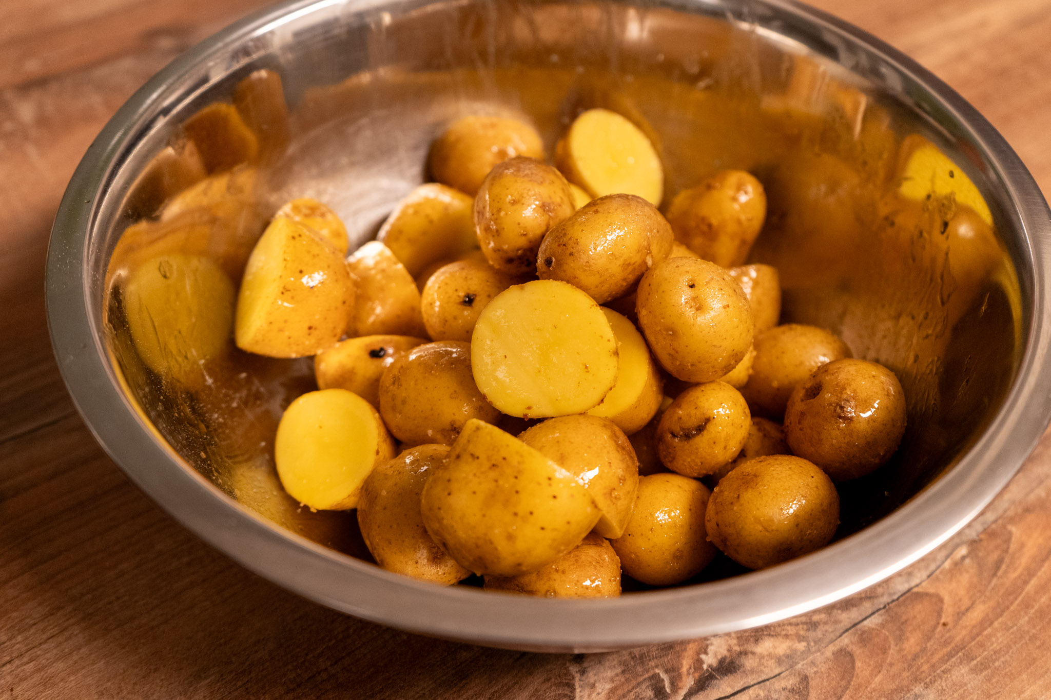 Schüssel mit geschnittenen und ganzen kleinen Kartoffeln auf einem Holztisch.