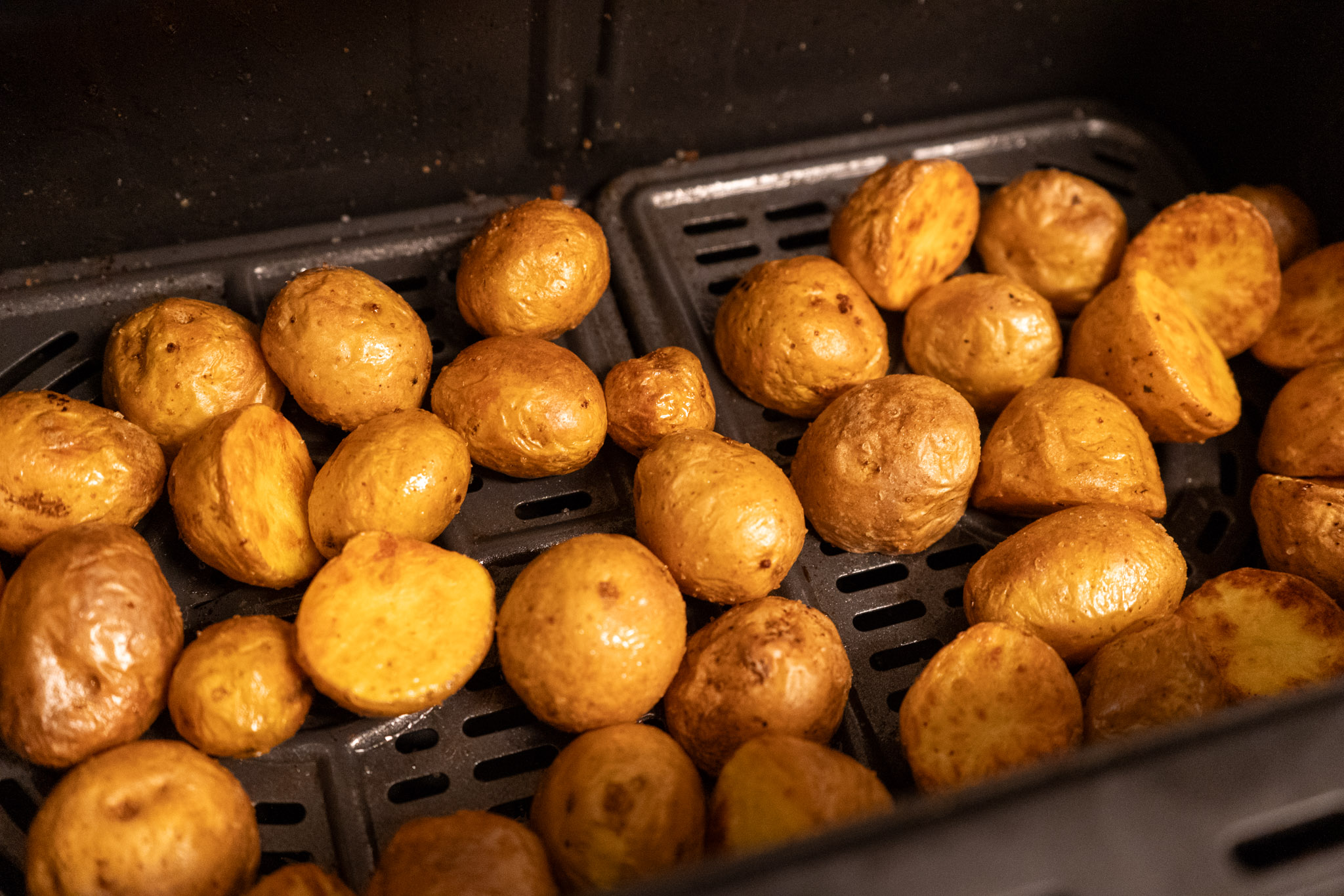 Ganze und halbe, goldbraun gebackene Kartoffeln in einer Heißluftfritteuse.