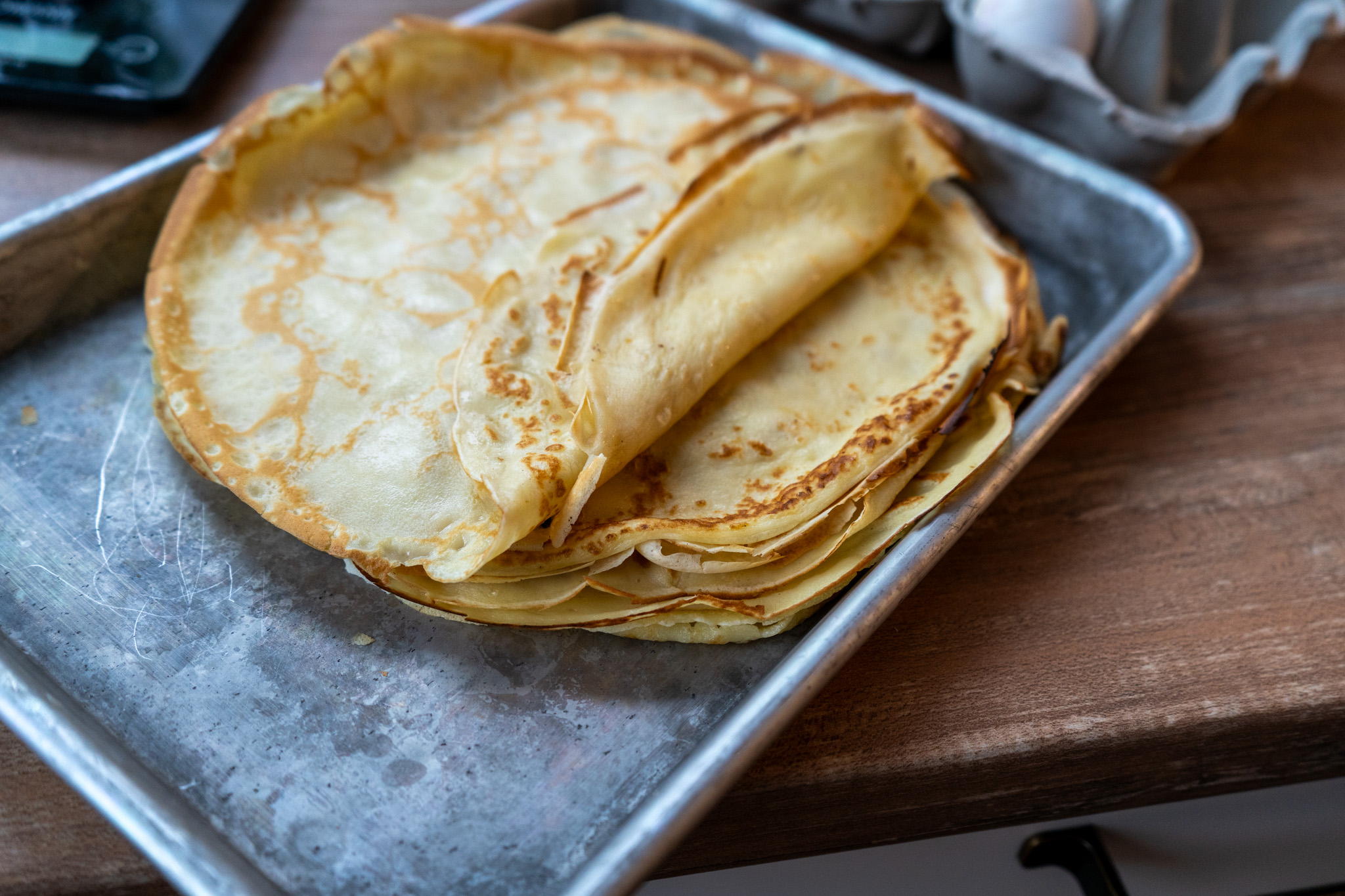 Französische-Crêpes_01 Ein Stapel frisch gebackener Crêpes auf einem Metallblech auf einem Holztisch.