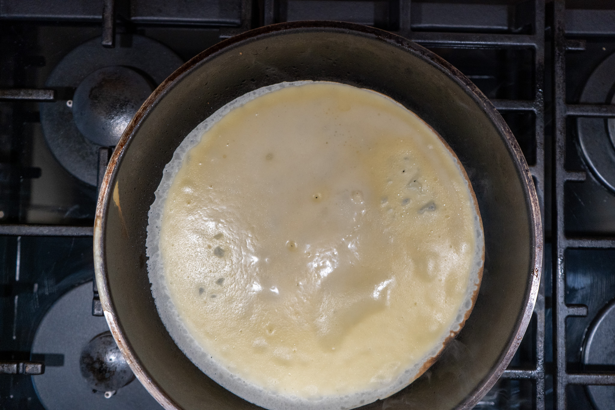 Französische-Crêpes_04 Pfannkuchen wird in einer Pfanne auf einem Gasherd gebraten, sichtbar von oben.