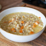 Schüssel mit Gemüsesuppe, darin Karotten- und weiße Bohnenstücke, auf einem Holzbrett serviert.