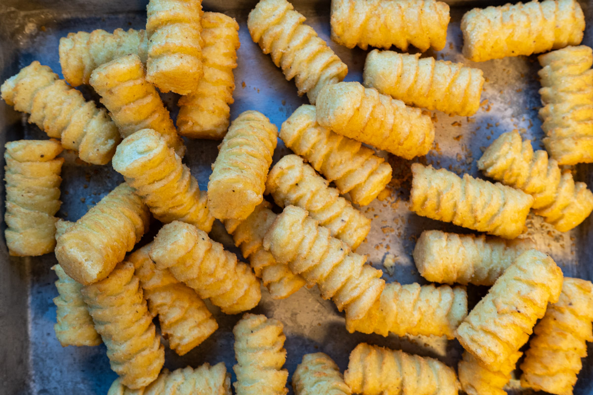 Heruntergefallene, goldbraune Kartoffelrösti auf einem metallenen Blech, von oben fotografiert.