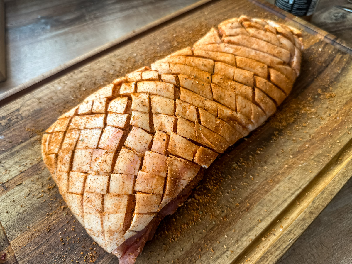 Krustenbraten-aus-Schweinebauch-aus-der-Heißluftfritteuse-03 Geritztes und gewürztes Schweinefleisch auf einem Holzbrett, bereit zum Kochen.