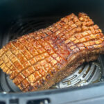 Knuspriger Schweinebraten in einer Heißluftfritteuse, mit goldbrauner, gerillter Kruste.