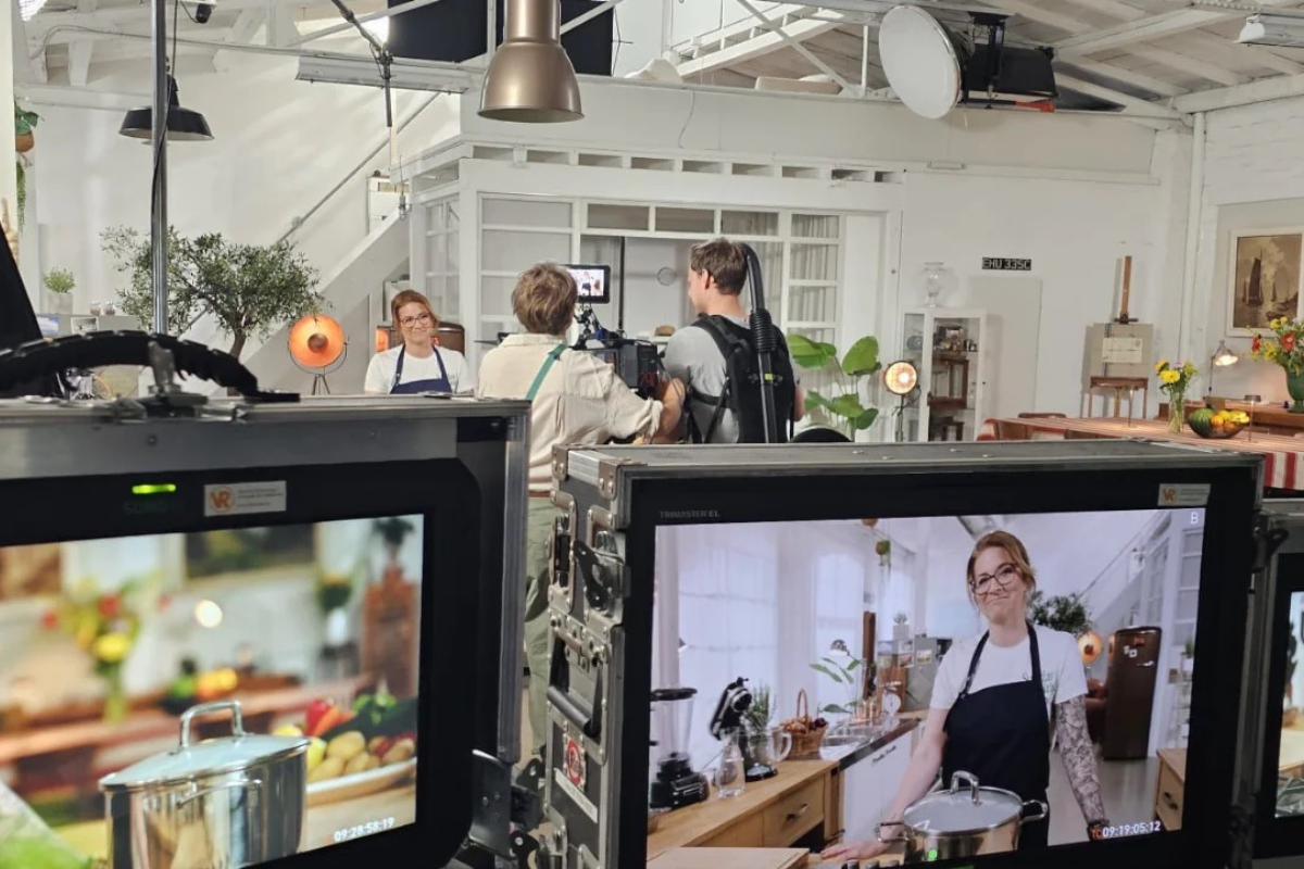 Dreh eines Kochvideos im Studio: Eine Frau in Schürze vor Kamera mit Monitoren im Vordergrund.