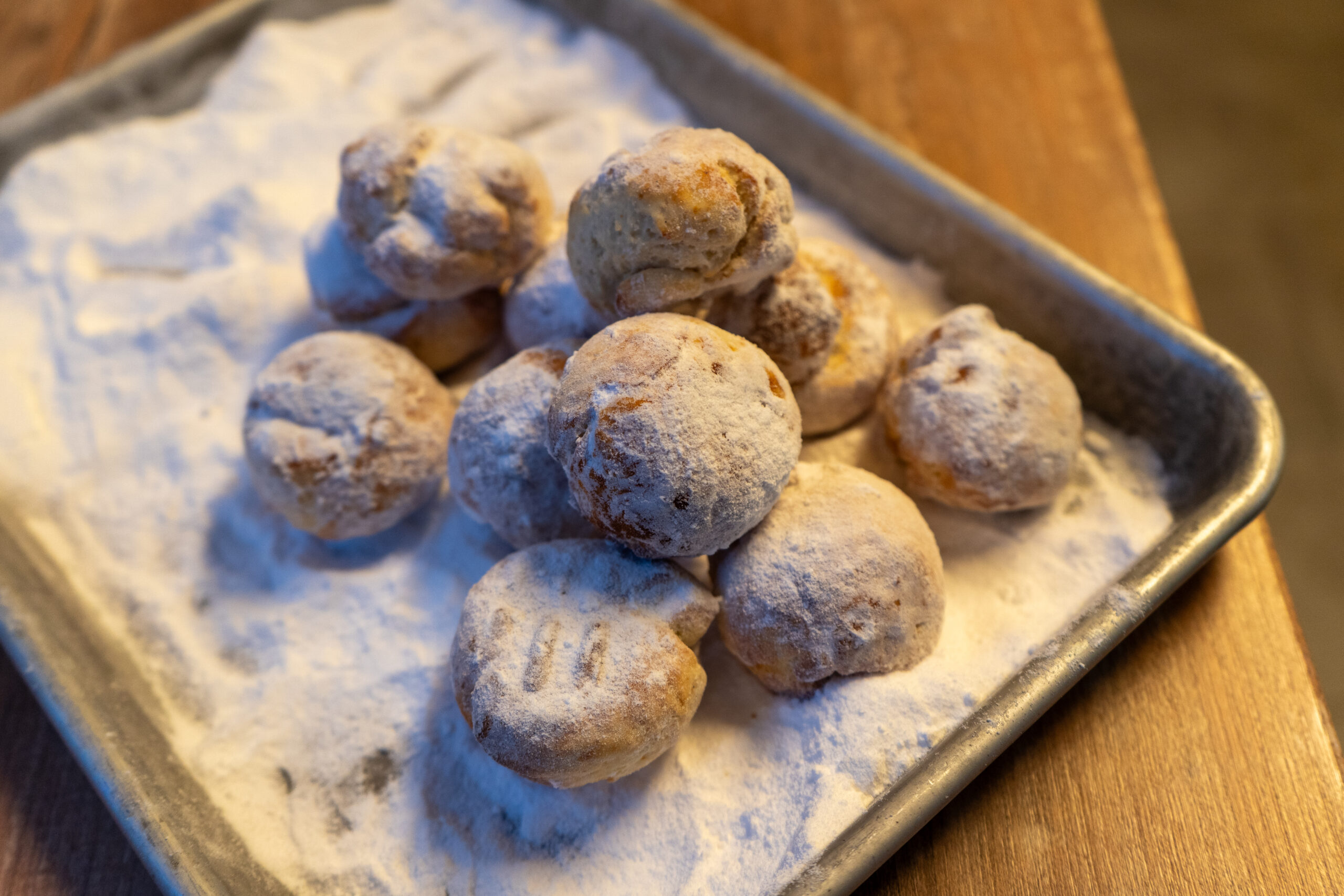 Tablett mit mit Puderzucker bestäubten Gebäckkugeln auf einem Holztisch.