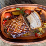 Gebackenes Schweinefleisch in einer Tonform, mit knuspriger Kruste, Tomaten und Rosmarin garniert.