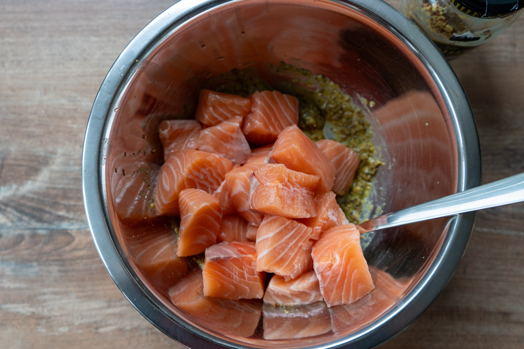 Lachs-Bites_03 Würfel von rohem Lachs in einer Metallschüssel, neben einer Marinade mit Gewürzen und einem Löffel.
