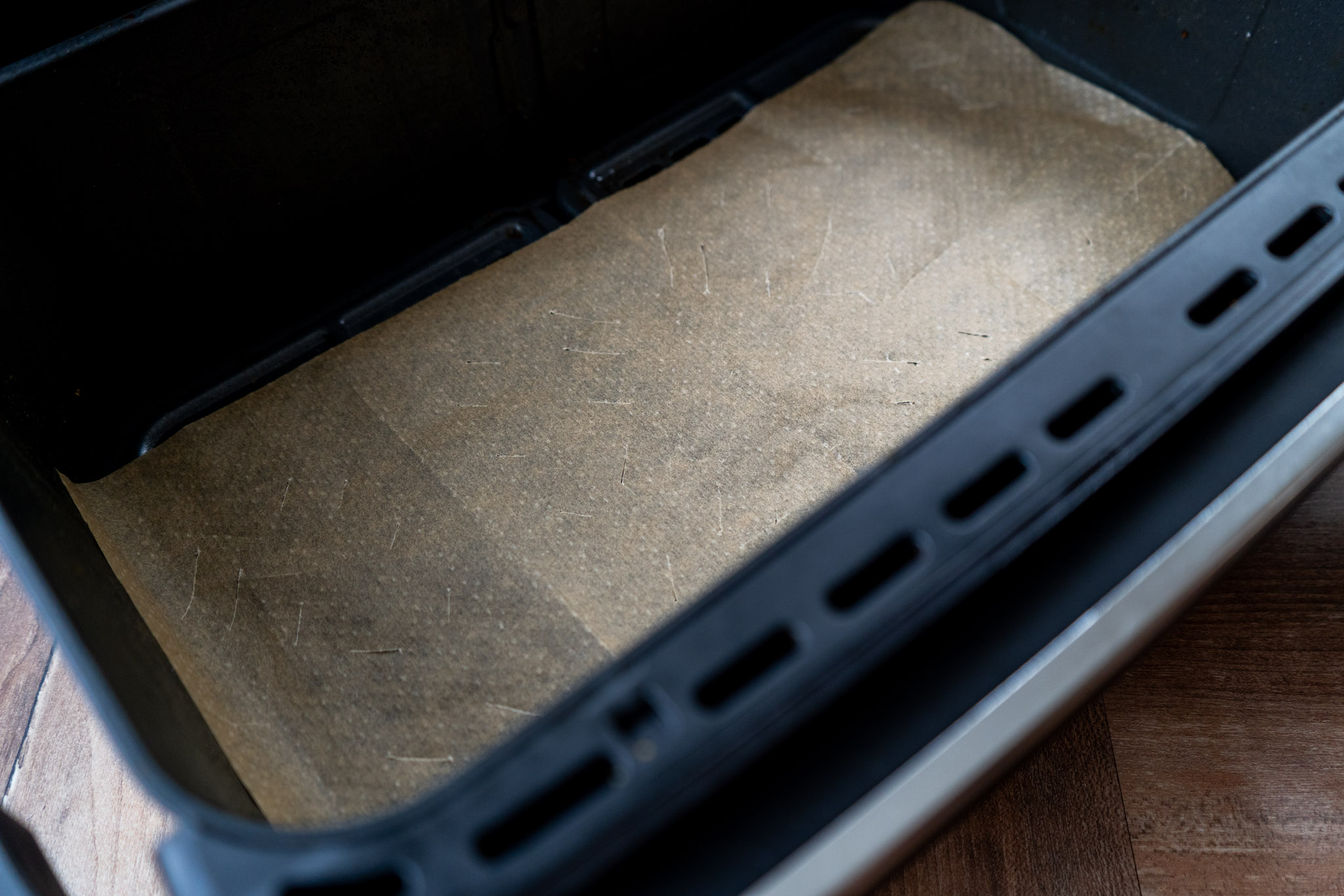 Lachs-Bites_02 Große schwarze Backform mit braunem Backpapier ausgelegt auf Holztisch.