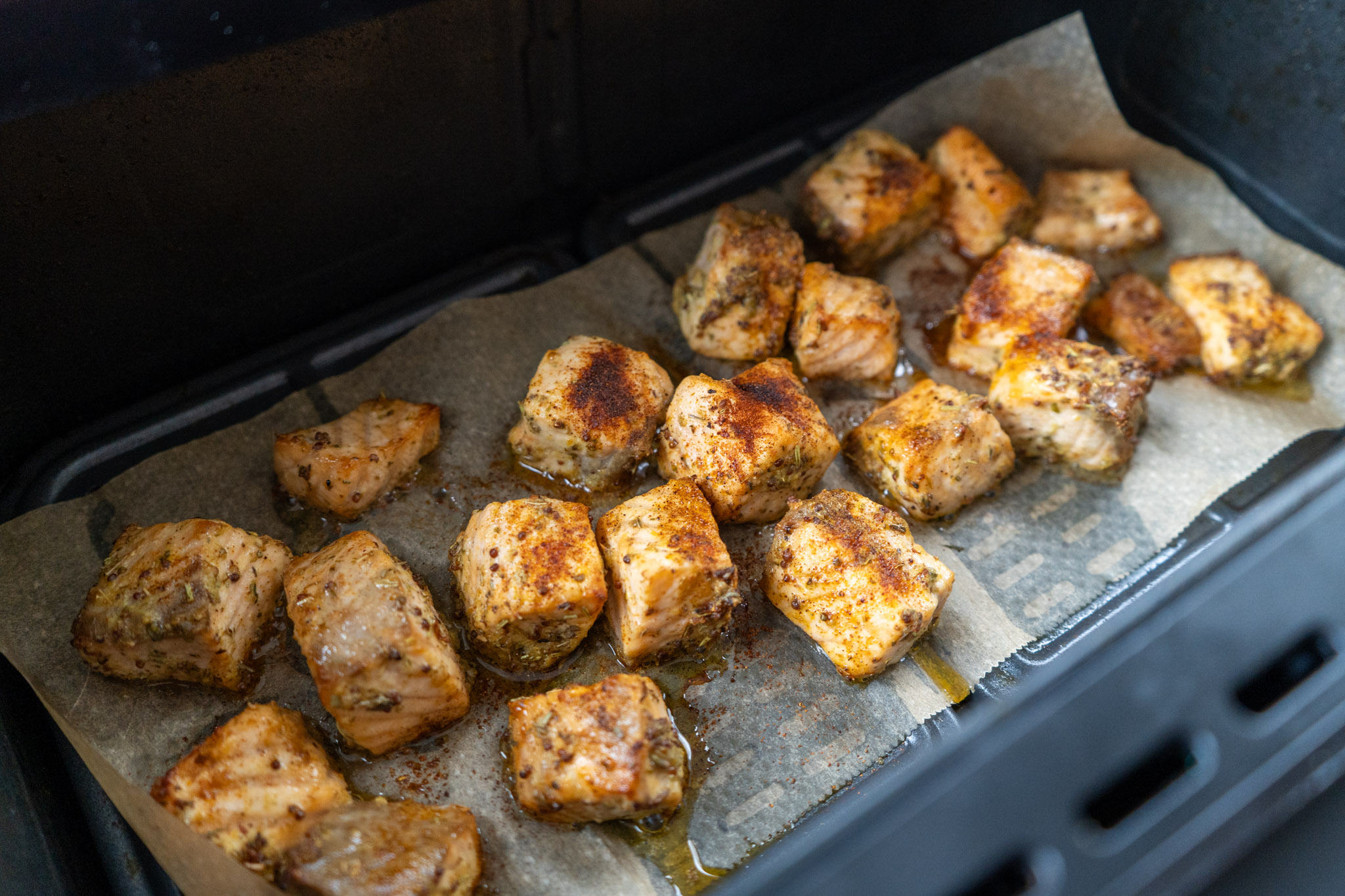 Lachs-Bites_04 Gewürzte Lachsfiletstücke auf Backpapier in einem Ofen gebacken.