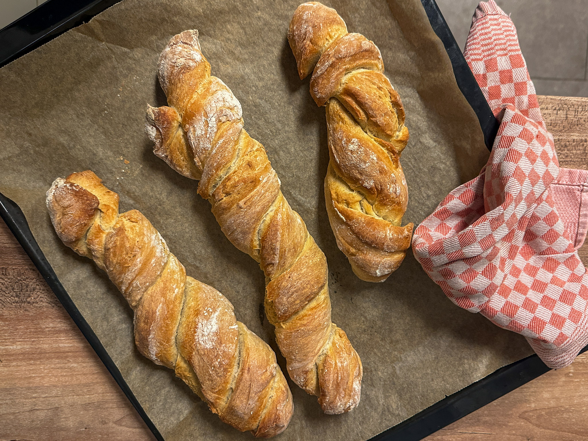 Frische, gedrehte Brote auf Backpapier mit einem Stück Butter und einem Messer daneben.