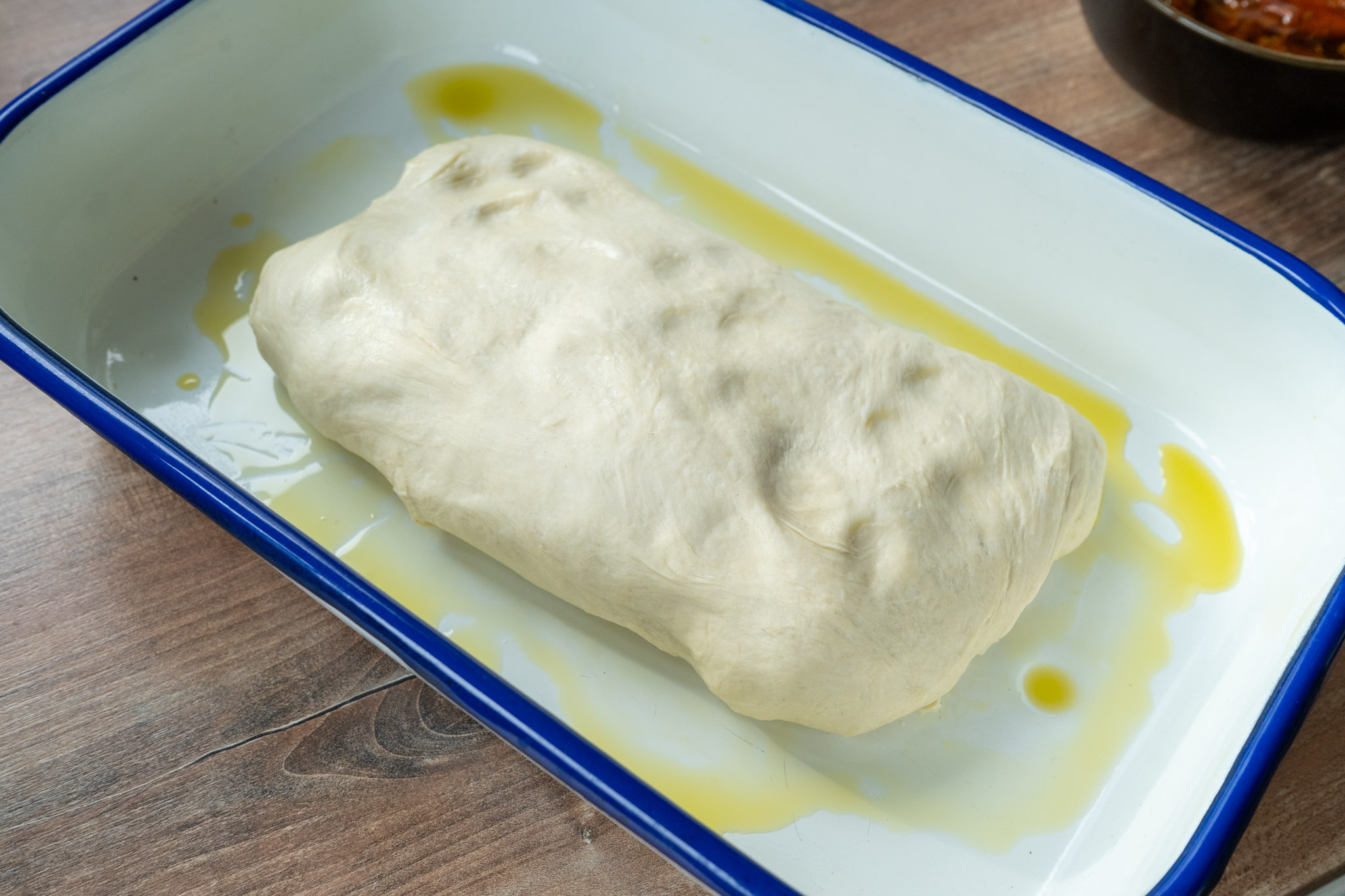 Teigrolle mit Öl in einer blauen Backform auf einem Holztisch.