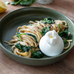 Nudeln mit Spinat und Pfeffer, serviert mit einer Kugel Burrata auf einem grünen Teller; Zitrone im Hintergrund.