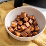 Schüssel mit gewürzten, gebratenen Tofuwürfeln auf gelbem Stofftuch.