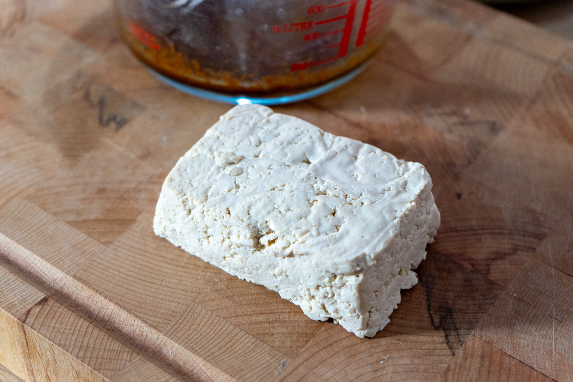 Knuspriger_Tofu_02 Schale mit Bohnensuppe auf einem Holzbrett, im Hintergrund ein Messer und geschnittene Zwiebeln.