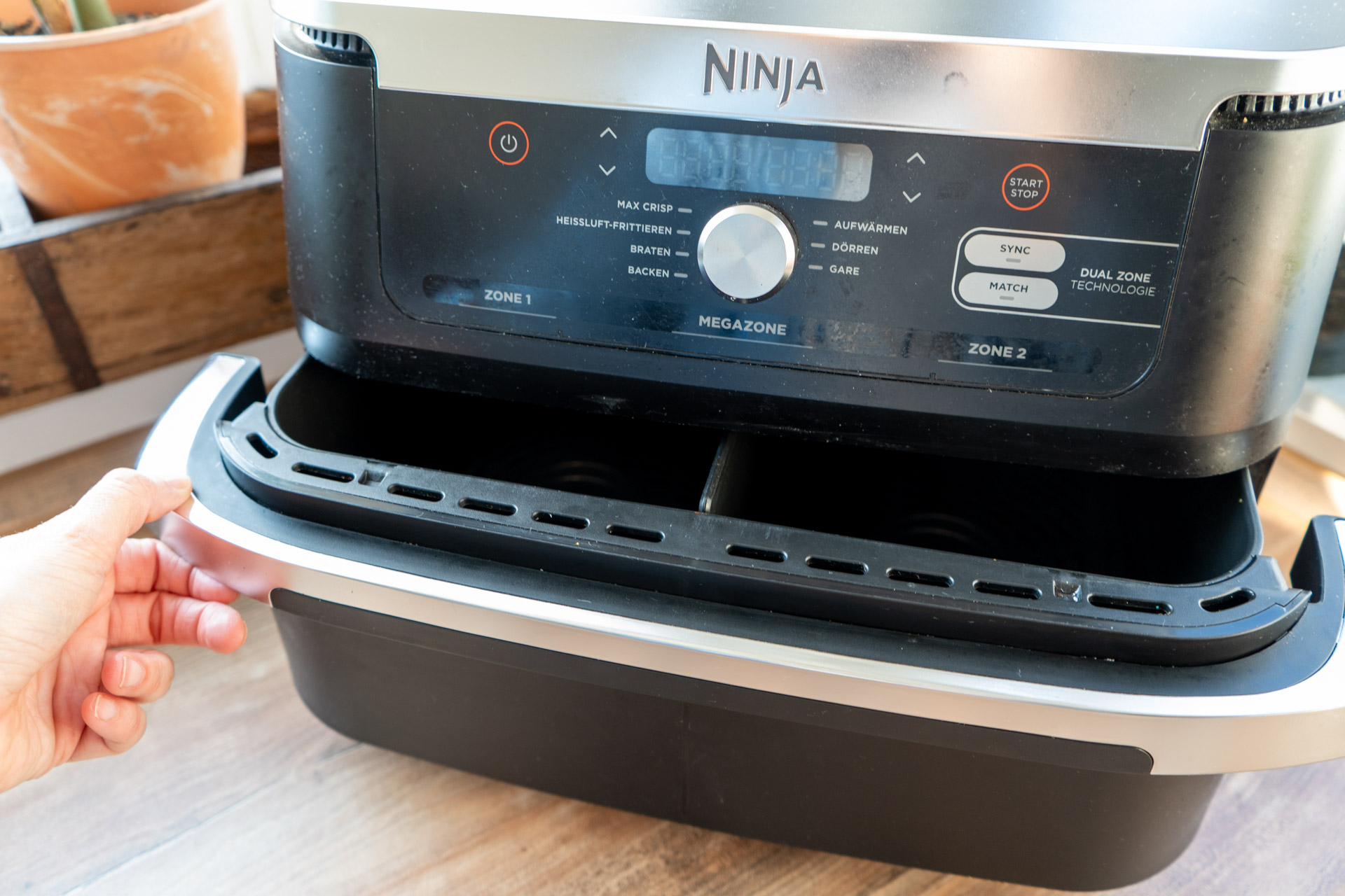 Ninja Foodi FlexDrawer AF500EU Test_02 Hand zieht Schublade eines Heißluftfritteuse-Geräts heraus, das auf einer Holzoberfläche steht.