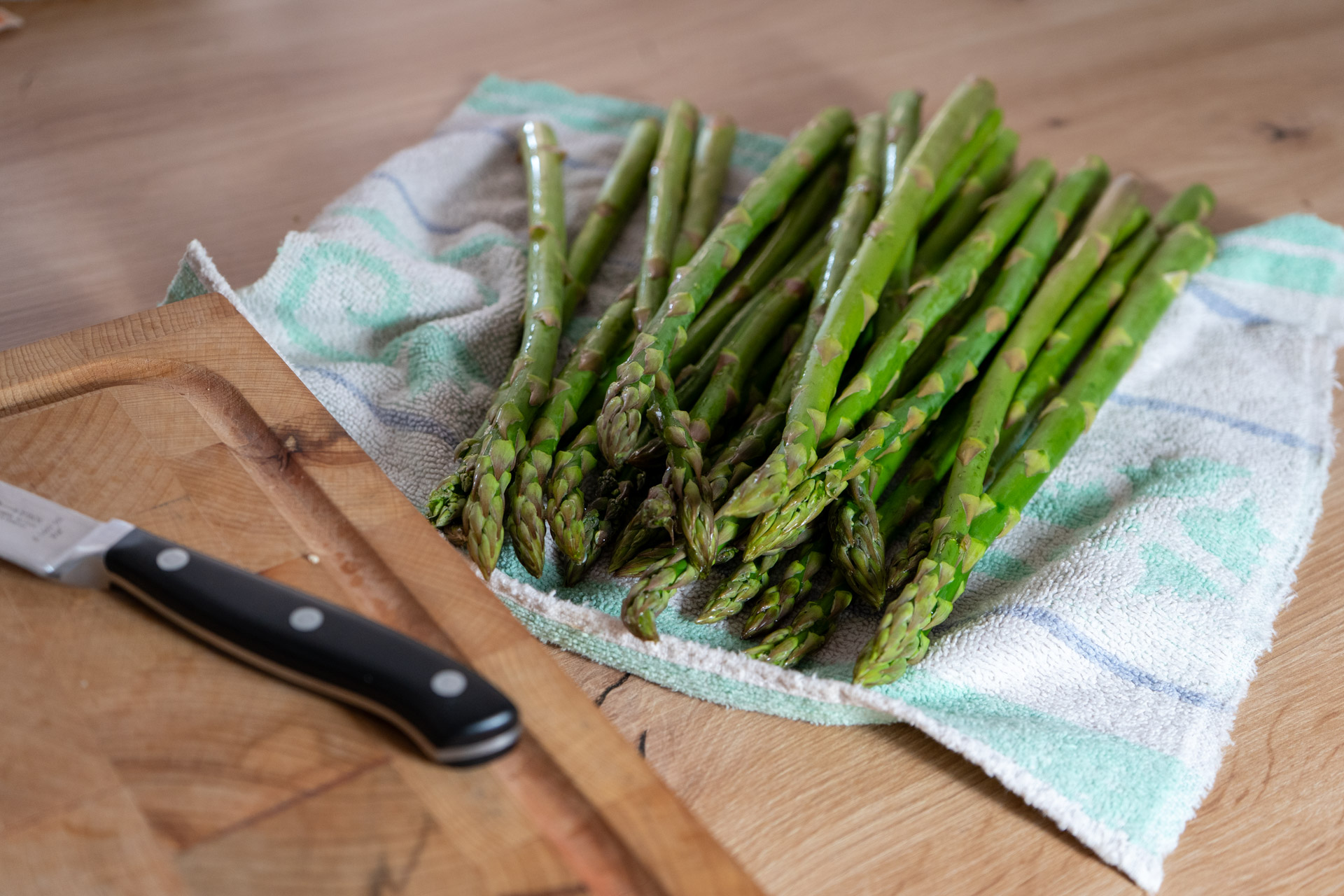 Grüner Spargel auf einem Handtuch, daneben ein Messer auf einem Holzbrett.