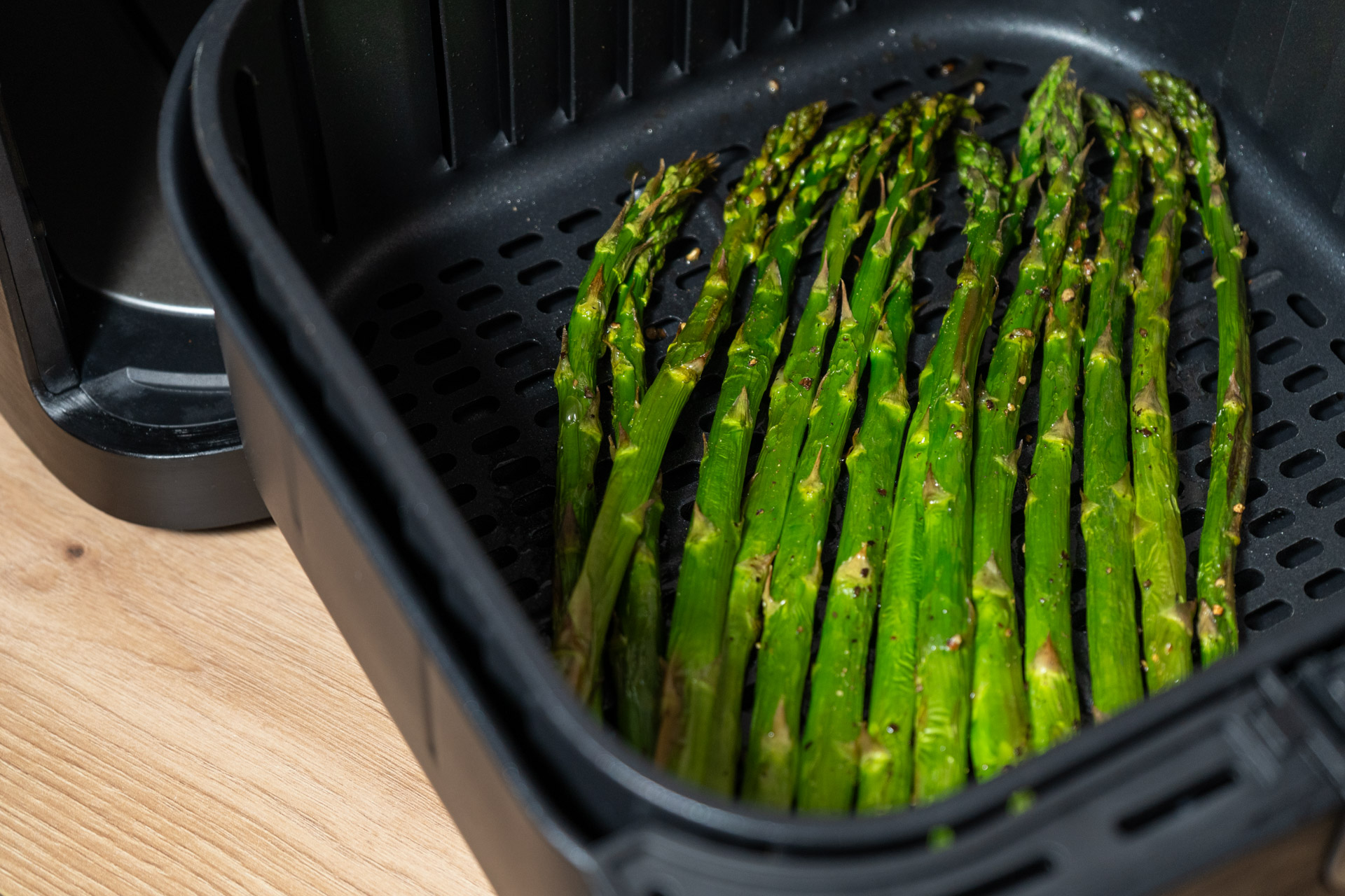 Grüner Spargel liegt in einer Heißluftfritteuse auf einer Holzoberfläche bereit zum Garen.