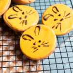 Kekse mit gelbem Zuckerguss und Schokogesichtern auf einem schwarzen Rost.