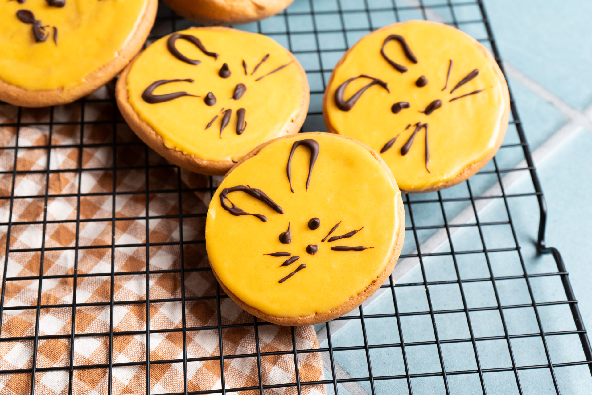 Kekse mit gelbem Zuckerguss und Schokogesichtern auf einem schwarzen Rost.