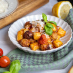 Teller mit Gnocchi und Fleischbällchen, garniert mit Basilikum und Parmesan, umgeben von Tomaten, Zitrone und geriebenem Käse.