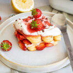 Dessert mit Löffelbiskuits, Sahne und frischen Erdbeeren auf einem Teller, dekoriert mit einem Löfel und halbierter Zitrone.