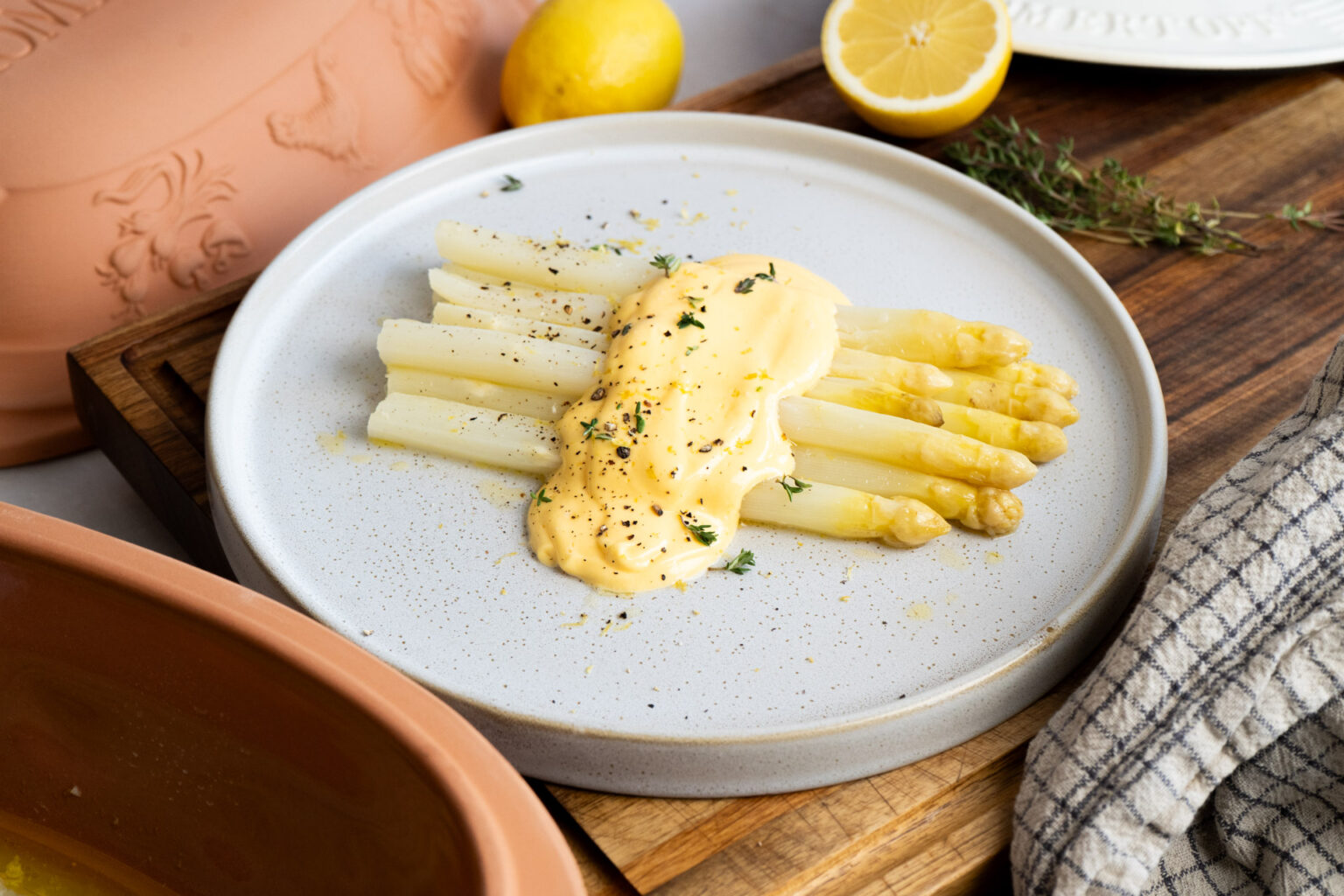 Weißer Spargel mit Sauce Hollandaise und frischen Kräutern, serviert auf einem weißen Teller, daneben halbe Zitrone.