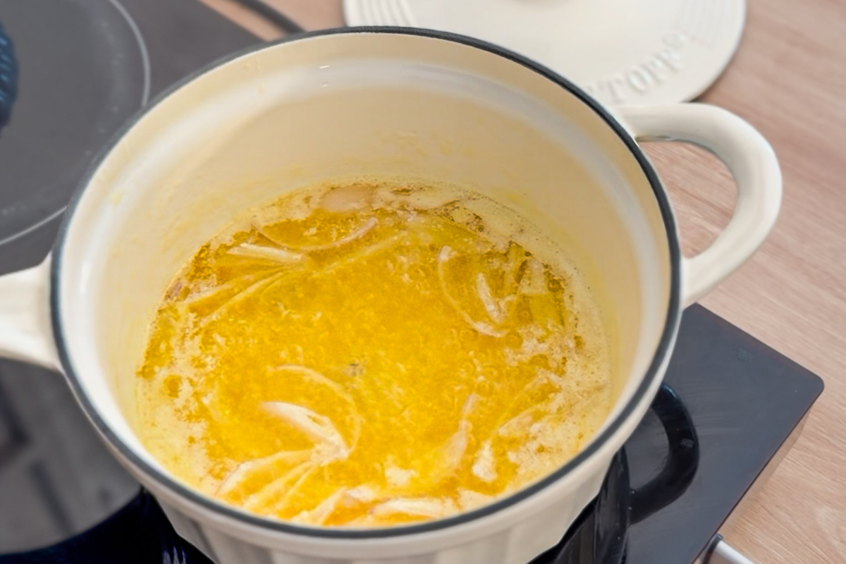 Topf mit schmelzender Butter und Zwiebelstücken auf einem Herd.