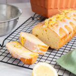 Zitronenkuchen mit Glasur und Zitronenzesten auf einem Kuchengitter, daneben eine Schüssel und eine halbierte Zitrone.