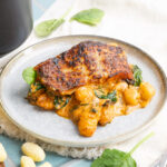 Gebackenes Stück Lachs auf cremigen Gnocchi mit Spinat, serviert auf einem Teller, daneben Gabel und Messer.