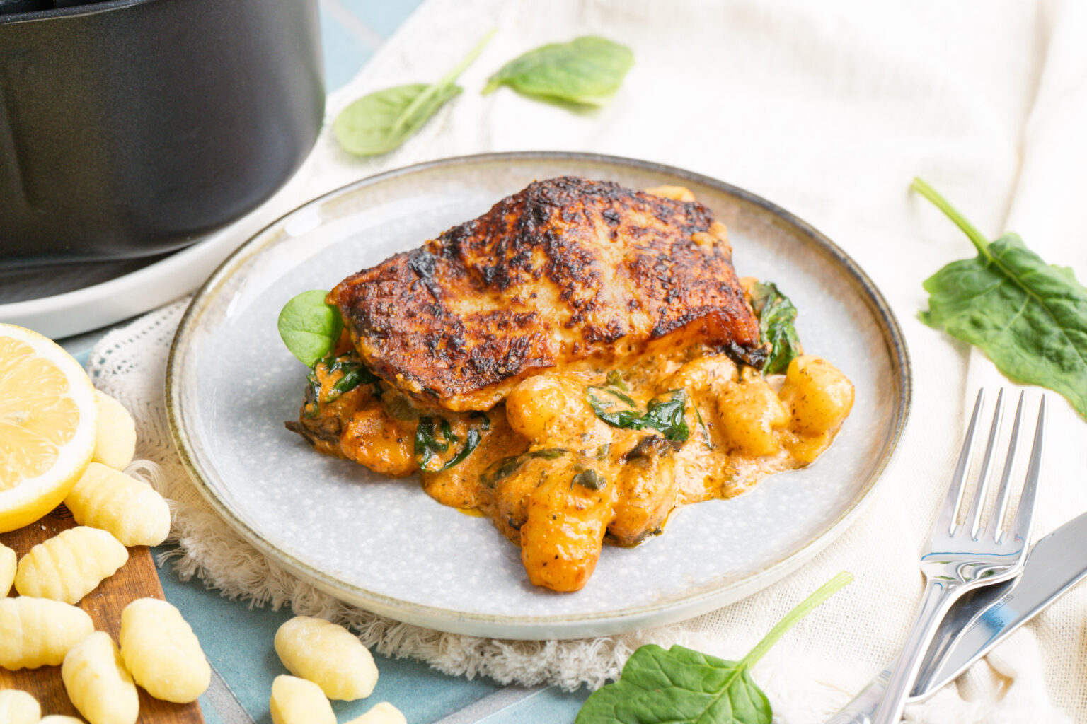 Gebackenes Stück Lachs auf cremigen Gnocchi mit Spinat, serviert auf einem Teller, daneben Gabel und Messer.