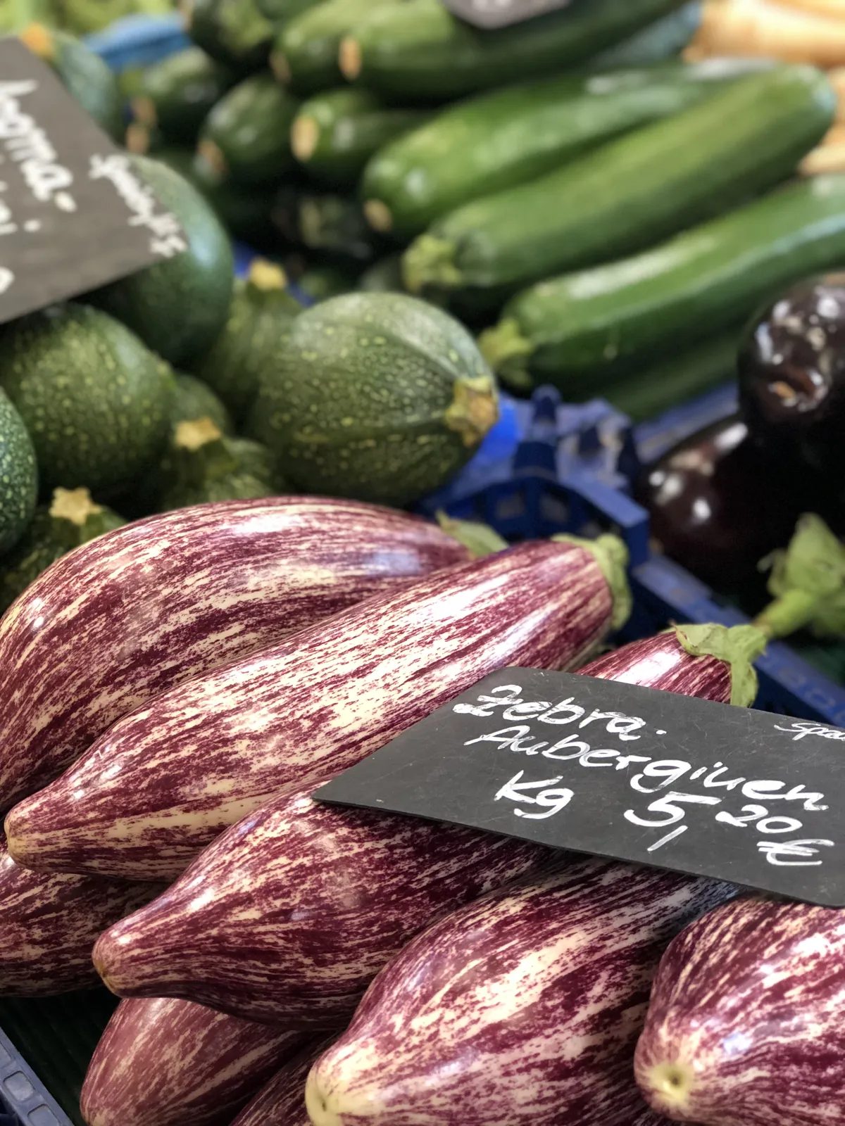 Gestreifte Zebra-Auberginen und Zucchini an einem Marktstand mit Preisschild.
