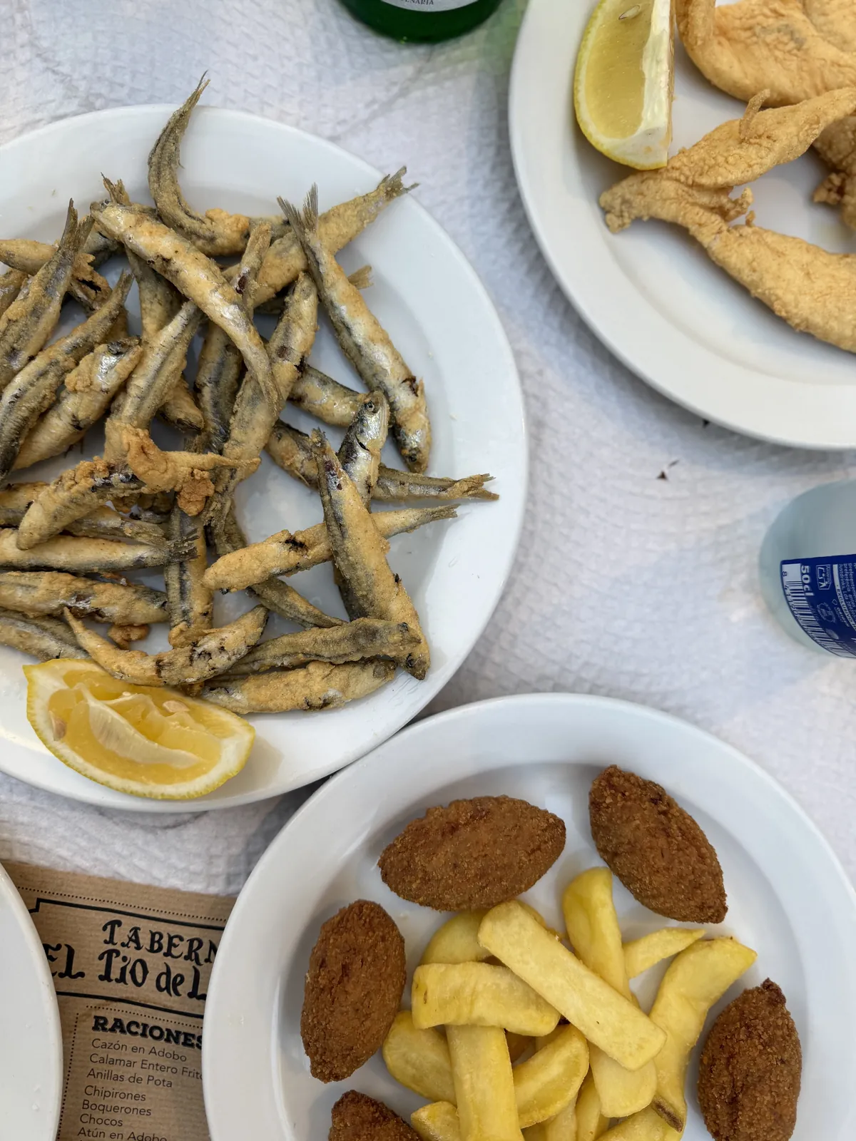 Teller mit frittierten Boquerones und Zitrone, daneben Croquetas mit Pommes und frittierter Fisch.