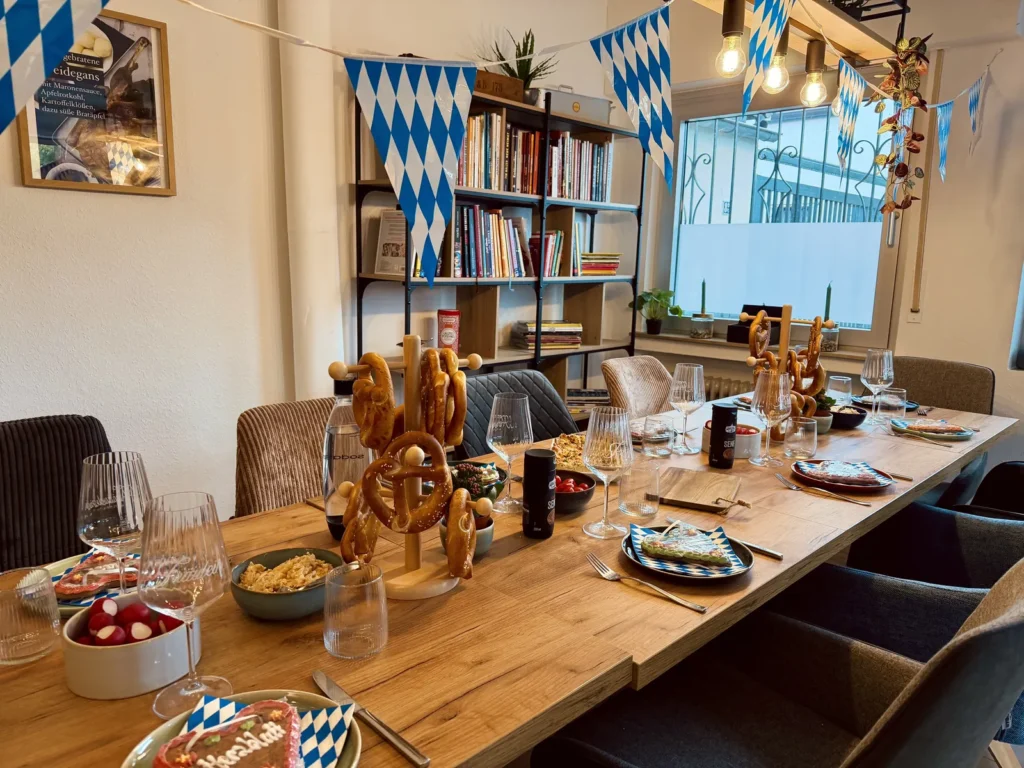 Gedeckte lange Tafel mit Brezeln, Weingläsern und blau-weißen Wimpeln