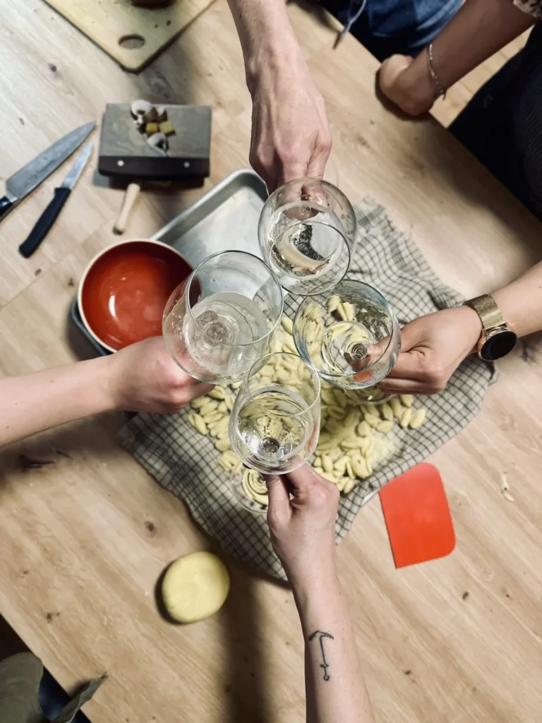 Hände beim Pastakurs mit Nudelteig und Weingläsern auf dem Holztisch