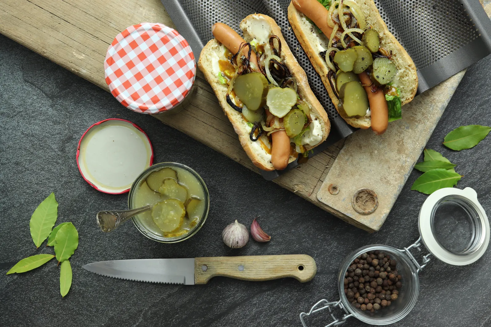 Zwei Hot Dogs mit eingelegten Gin-Gurken und Röstzwiebeln auf dunklem Untergrund, von oben fotografiert.