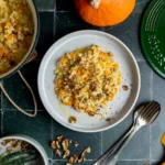 Kürbisrisotto mit Walnüssen auf einem weißen Teller, daneben ein grüner gusseiserner Topf mit Risotto, Hokkaido-Kürbis und Thymian, von oben fotografiert.