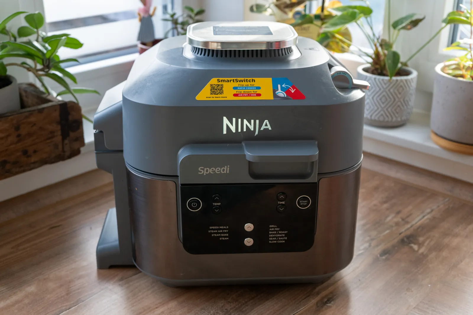 Ninja Speedi ON400EU in Grau auf einer Holzarbeitsplatte vor einem Fenster mit Zimmerpflanzen.
