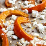 Gebackene Kürbisspalten mit zerbröseltem Feta, Honig und Chiliflocken auf einem Backblech mit Backpapier