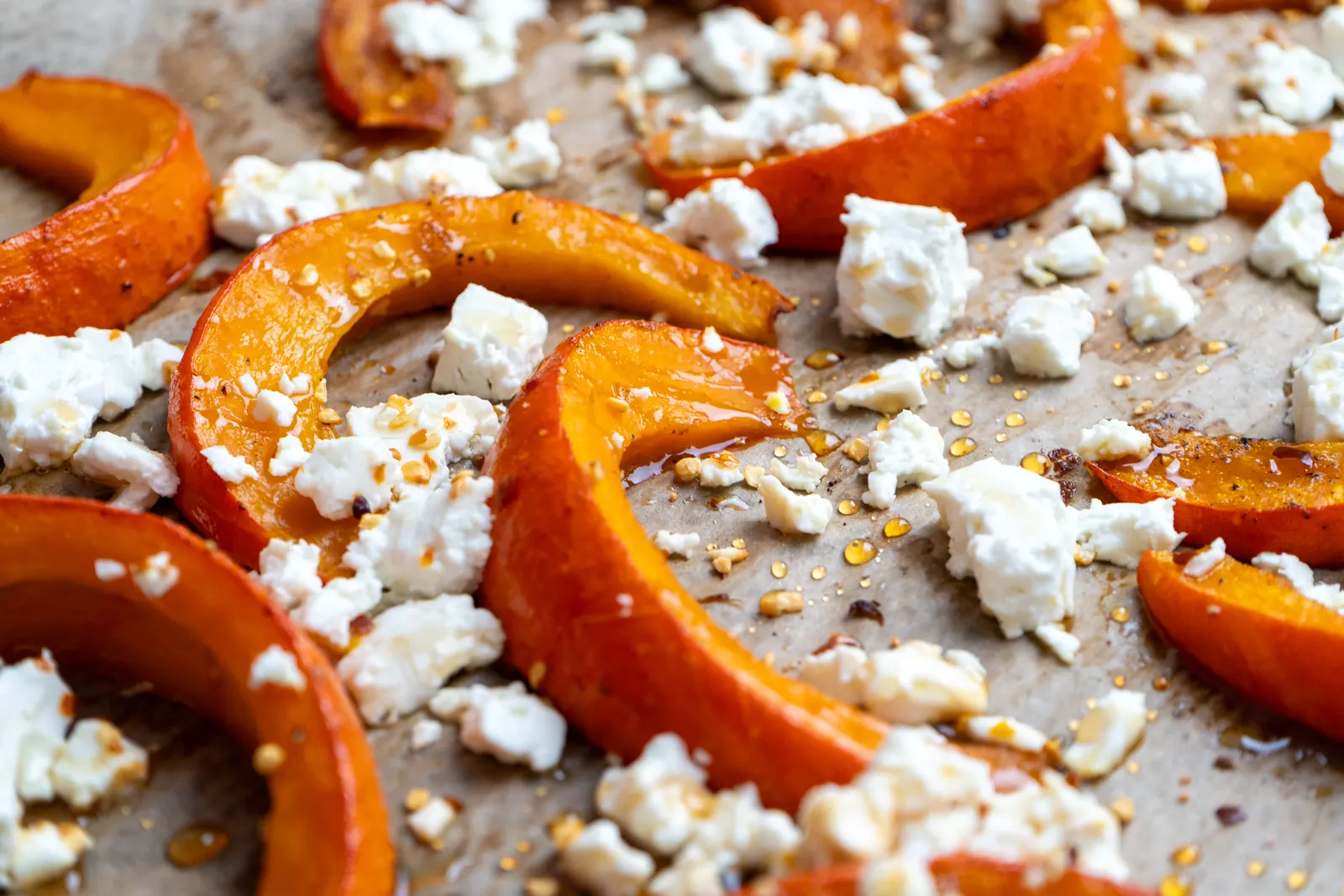Gebackene Kürbisspalten mit zerbröseltem Feta, Honig und Chiliflocken auf einem Backblech mit Backpapier