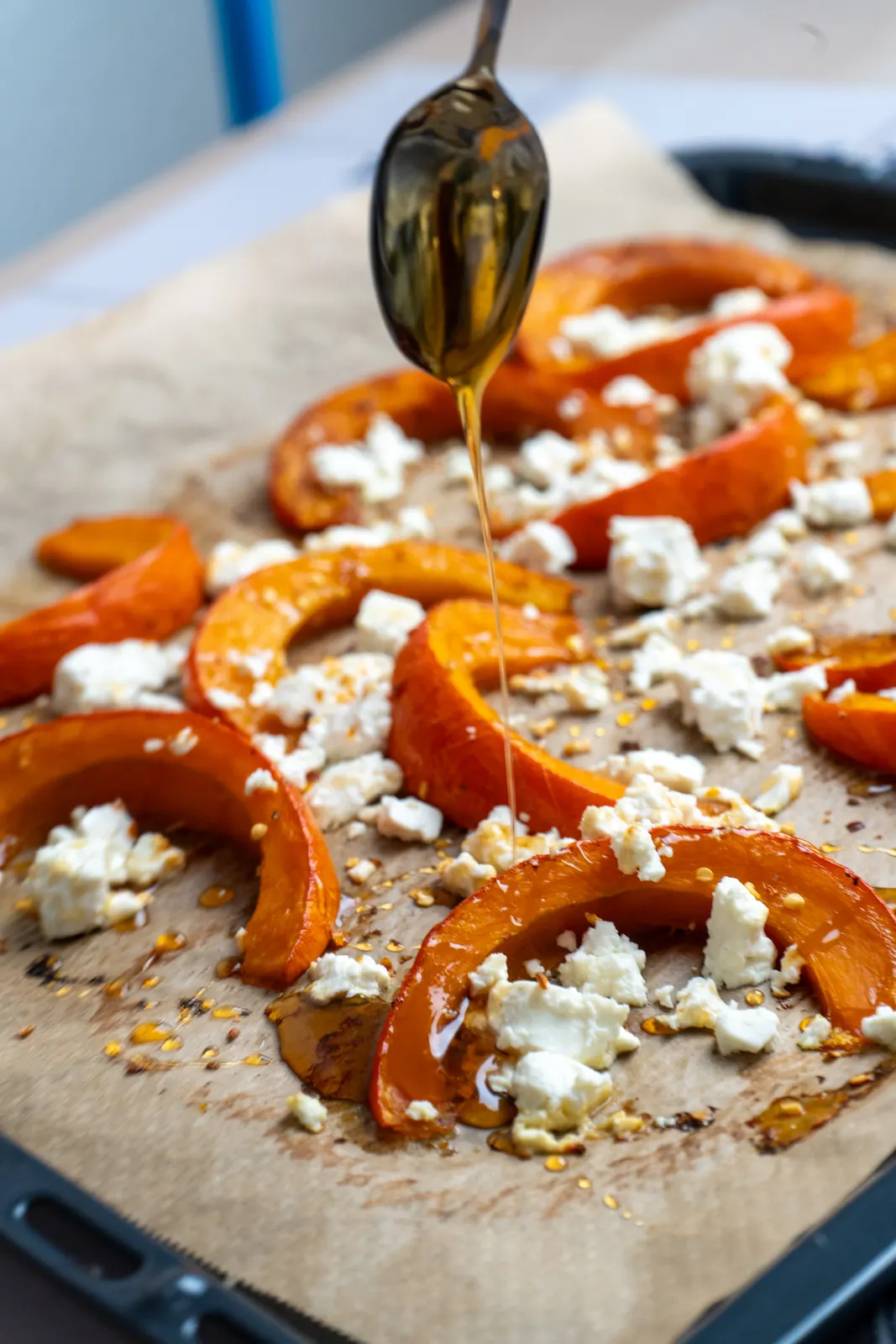 Honig wird mit einem Löffel über gebackene Kürbisspalten mit Feta geträufelt