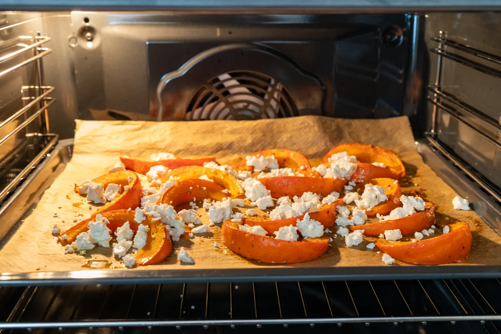 Kürbisspalten mit Feta auf einem Backblech im Backofen