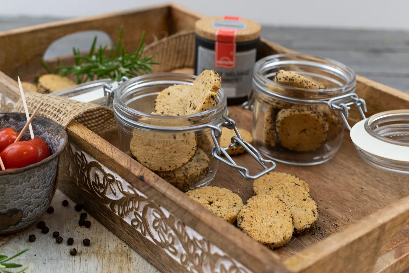 Pfeffer-Gebäck in Bügelgläsern auf einem Holztablett, daneben Cocktailtomaten und Rosmarin.
