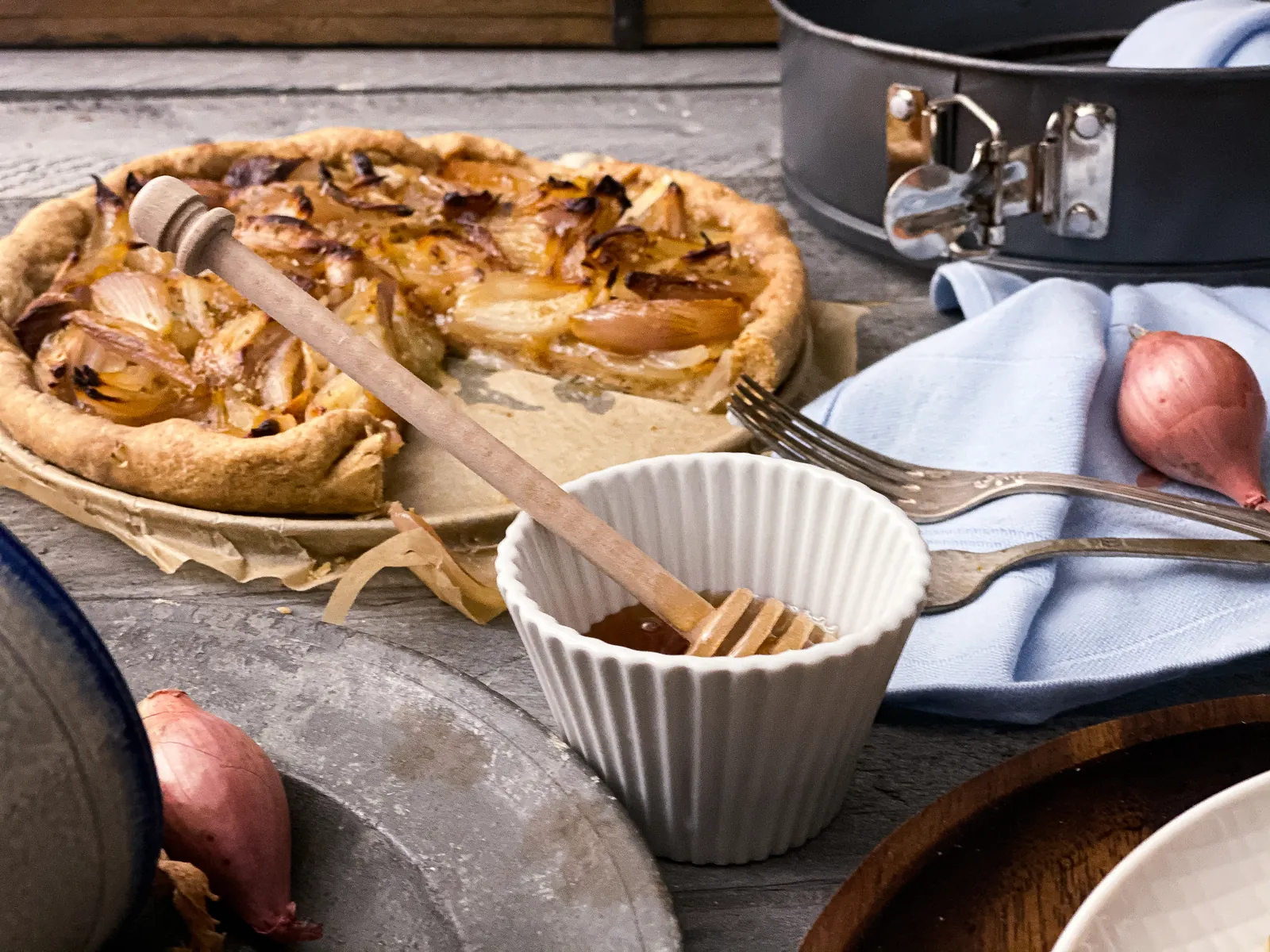 Zwiebelkuchen mit Schalotten und Honig, angeschnitten, daneben die Springform und ein Schälchen.