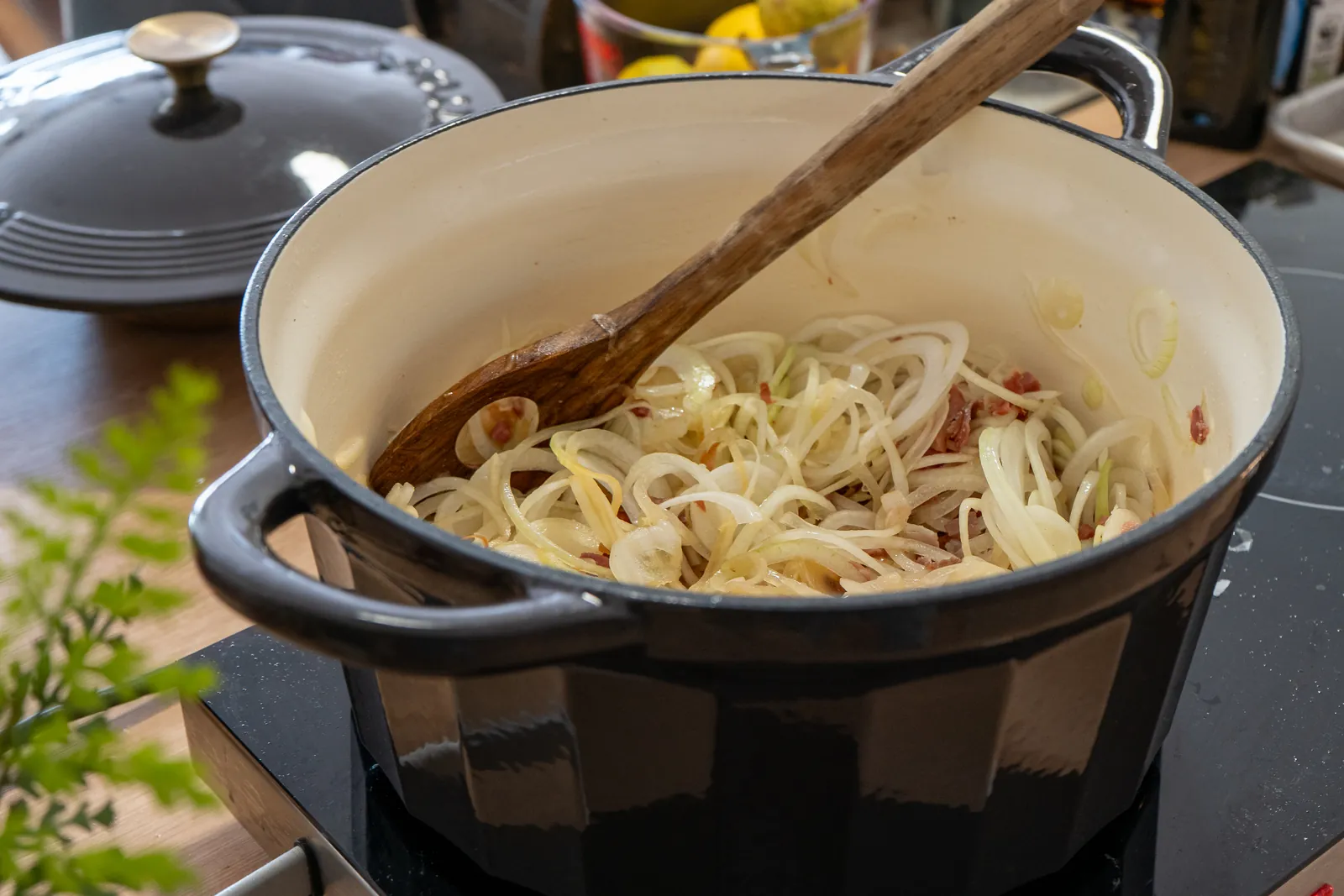 Zwiebelringe mit Speck werden in einem Topf mit einem Holzlöffel glasig gedünstet.